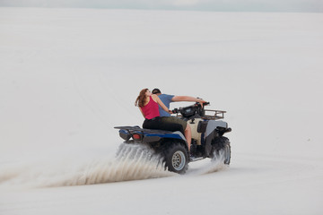 The guy and the girl ride a quad bike in the desert, having fun and enjoying, a couple of lovers