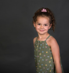 Beautiful smiling mixed race little girl with curly brown hair isolated on gray background