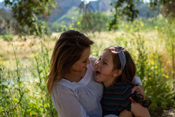 Latina Woman and daughter smiling together in front of a bright field at a park