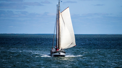 Big sailing yacht with two white sails filled with a wind sailing in the blue North sea