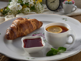 Croissant,jam ,tea with lemon, on a porcelain dish