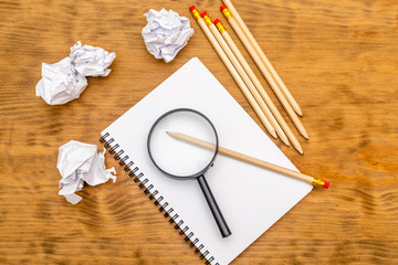 White note pad on a wooden table. Around the notepads lies lot crumpled paper