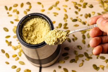 Pumpkin seeds in a coffee grinder. Pumpkin seeds powder in a spoon. Standing on a wooden table....