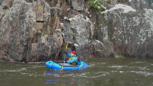 male paddler is paddling inflatable packraft upstream of a mountain river in early spring snowstorm, Poudre River in northern Colorado