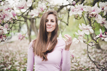 Fototapeta premium Cheerful long hair young woman under the blooming magnolia.