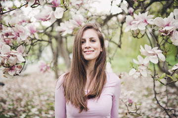Cheerful long hair young woman under the blooming magnolia.