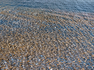 Stones on the lake bottom with sunshine reflection on the water