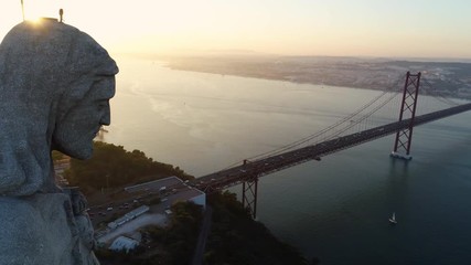 Aeria view monument Sanctuary of Christ the King. Drone flyby past near giant sculpture close up stone head in shining overlooking city of Lisbon Almada and famous 25th april bridge at sunset