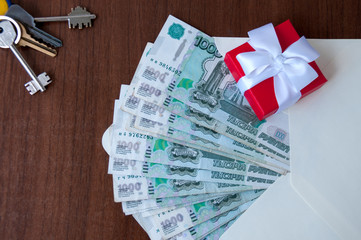 On the table is a red box with a white bow on the envelope with Russian banknotes in denominations of one thousand rubles and a bunch of keys