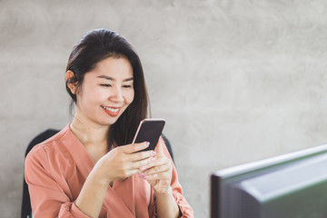 happy Asian woman make money online from smart phone with computer on desk 