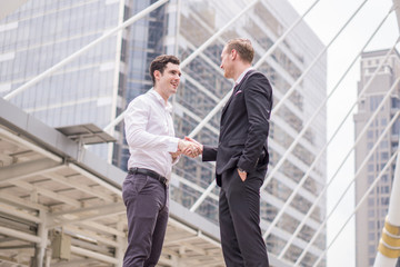 Two young businessmen shaking hands amid the surrounding buildings as a background