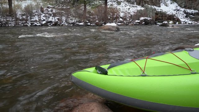 inflatable whitewater kayak wobbling on a shore of mountain river after springtime snowstorm - Poudre River in northern Colorado