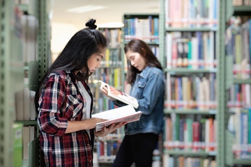 Asian female student open and learning textbook from bookshelf in the International College/University Library.