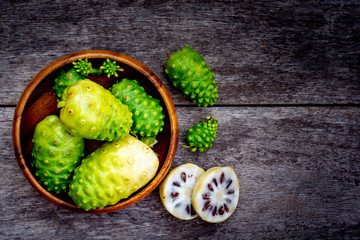 Fresh raw and ripe Morinda citrifolia or Noni fruit and sliced with seeds in wooden bowl isolated on white background.