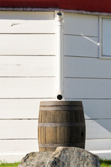 Wooden barrel in front of a pipe, coming down from a white striped wall. 
