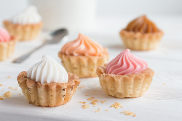 Small cakes and with cream on a white table with a spoon and a mug. Selective focus. 