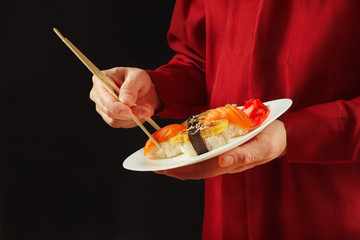 Hands of man in a red shirt takes sushi from the plate on a black background