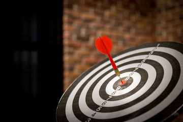 Red dart arrow hitting in the target center of dartboard on bullseye with sun light vintage style,...