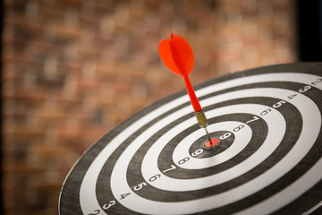 Red dart arrow hitting in the target center of dartboard on bullseye with sun light vintage style,...