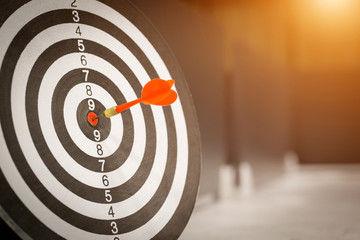 Red dart arrow hitting in the target center of dartboard on bullseye with sun light vintage style,...
