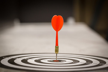 Fototapeta premium Red dart arrow hitting in the target center of dartboard on bullseye with sun light vintage style, Target marketing and business success concept - Image.