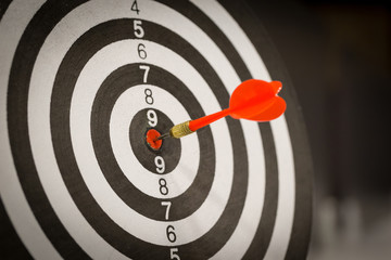 Red dart arrow hitting in the target center of dartboard on bullseye with sun light vintage style,...