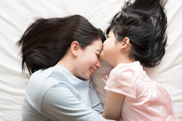 Daughter kisses her mother's forehead. and hugging in the bedroom .Happy Asian family