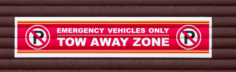 Obraz premium red and white no parking tow away sign for emergency vehicles only on brown background