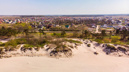 Fototapeta premium Amazing aerial view of the village with a lot of greenery, next to the sand dunes on a bright sunny day