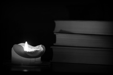 Burning candle and old books in the dark close up. Black and white