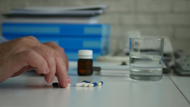 Man in Office Room Suffering a Big Headache Select Medical Pills from the Tabel