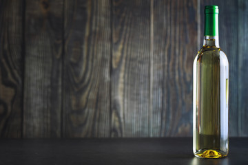 Transparent bottle of white dry wine on the table. White wine glass on a wooden background.