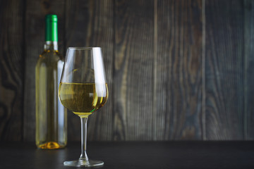 Transparent bottle of white dry wine on the table. White wine glass on a wooden background.