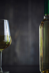 Transparent bottle of white dry wine on the table. White wine glass on a wooden background.