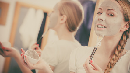 Happy young woman applying mud mask on face