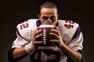 Portrait of american football player holding a ball and looking at camera
