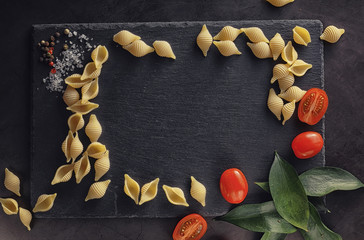 Pasta shells on black stone. Tomatoes and bay leaves with allspice and sea salt.