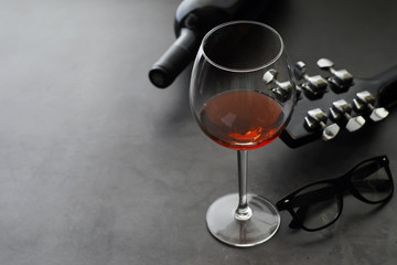 Guitar and high glass with red wine on a stone background.