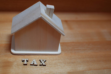 Obraz na płótnie Canvas Tax - word and house model on wooden background with copy space. Taxes on real estate, property tax concept.
