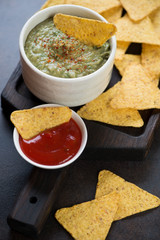 Close-up of nachos and dipping sauces on a black wooden serving tray, vertical shot, selective focus