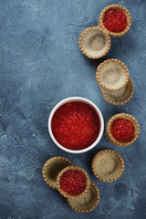 Above view of tartlets with red caviar over blue stone background, vertical shot with copy space