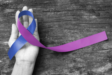 Blue purple ribbon on human hand aged wood background for RA rheumatoid arthritis illness disease - obrazy, fototapety, plakaty