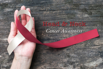 Head and neck cancer awareness with symbolic burgundy ivory white color ribbon on hand with old...