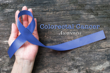Colorectal or Colon cancer awareness dark blue ribbon on helping hand on old aged woo
