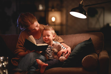 Family before going to bed mother reads to her child son book near a lamp in the evening.