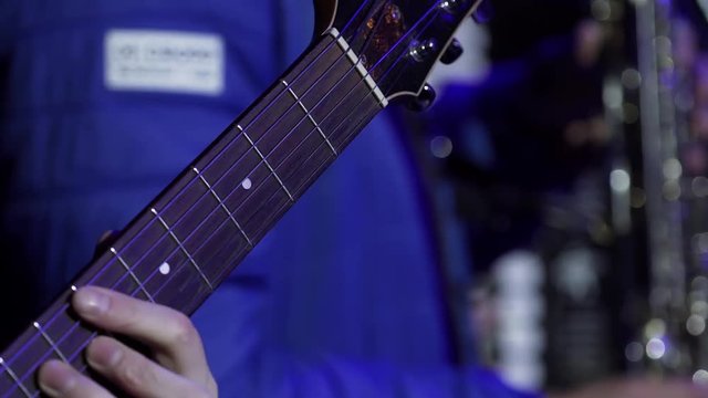 Male musician wearing black outfit professionally beautiful acoustic guitar standing on stage with other musician dressed in blue outfit during some concert performance.