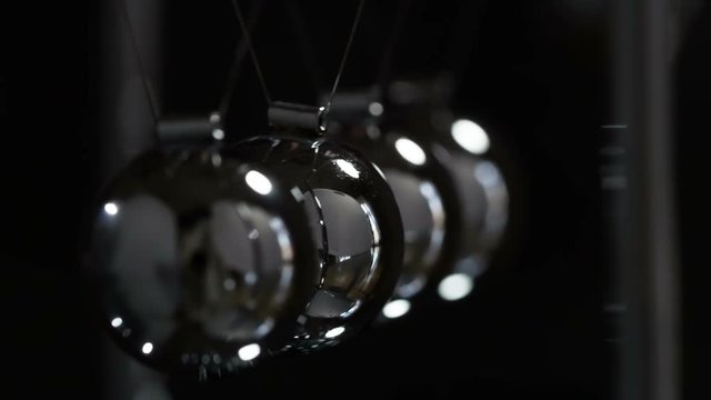 Slow Motion of Newton Balls. Loop. Steel shiny balls suspended on a dark background. They interact with each other, transferring the force of impact. Filmed at a speed of 240fps
