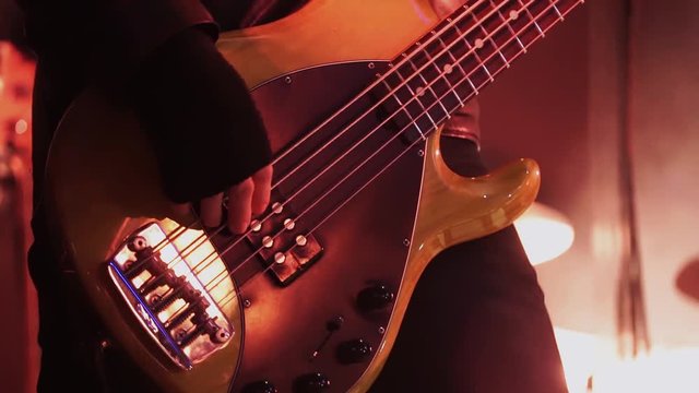 Man guitar player wearing black leather tight jacket professionally and joyfully plays cute bass guitar standing on stage during concert performance.