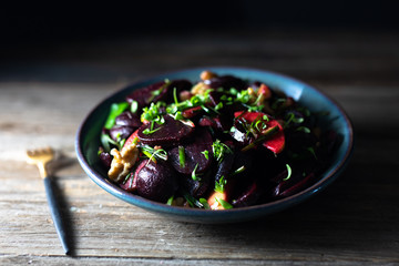 Roasted beet/beetroot, apples, walnuts, microgreens, winter salad, scallions salad in a blue pottery bowl with homemade vinaigrette and golden spoon on rustic wooden table