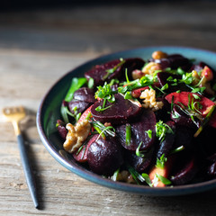 Roasted beet/beetroot, apples, walnuts, microgreens, winter salad, scallions salad in a blue pottery bowl with homemade vinaigrette and golden spoon on rustic wooden table. 